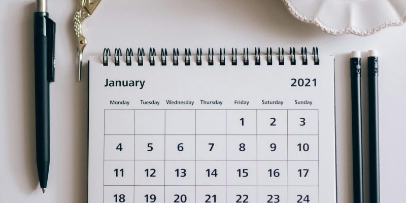 Flat lay of a 2021 desk calendar, coffee cup, and black stationery items on a white surface.